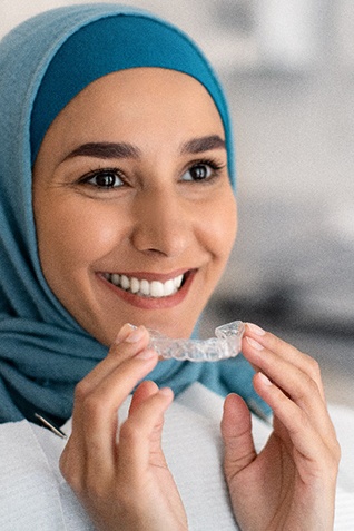 Woman smiling while holding SureSmile aligner