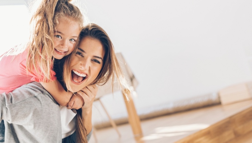 Laughing mother giving young daughter piggyback ride