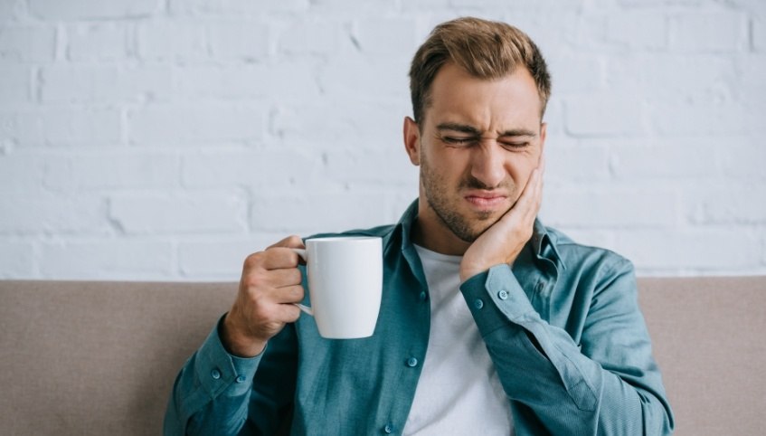 Man with coffee mug holding his cheek in pain needing emergency dentist in Arundel