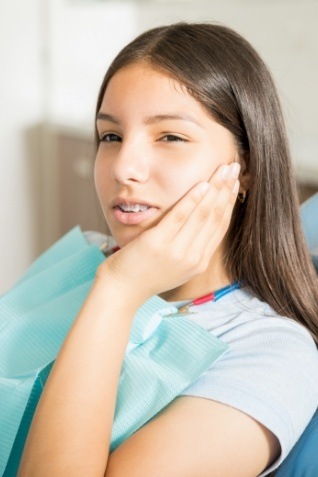 Young woman holding side of face in pain while visiting emergency dentist in Arundel
