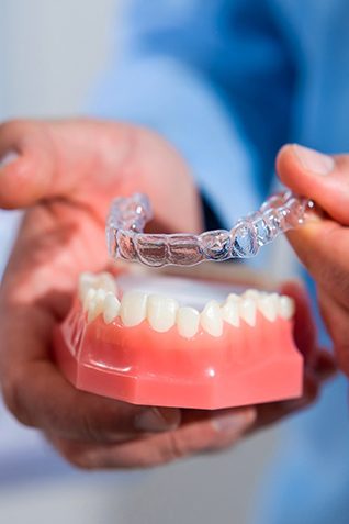 Dentist placing clear aligner on model of teeth