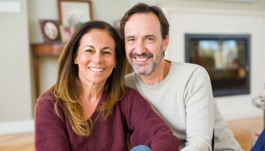Older man and woman smiling in their living room after replacing missing teeth in Arundel