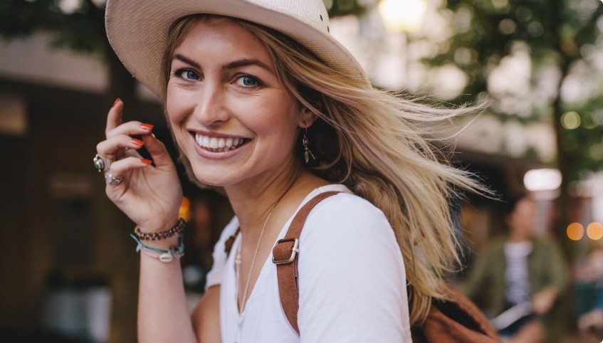 Woman in sunhat smiling outdoors after receiving dental services in Arundel