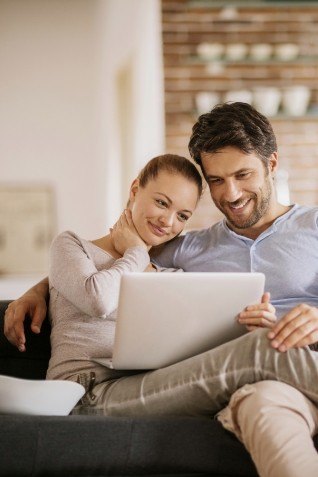 Man and woman looking at laptop while cuddling on couch