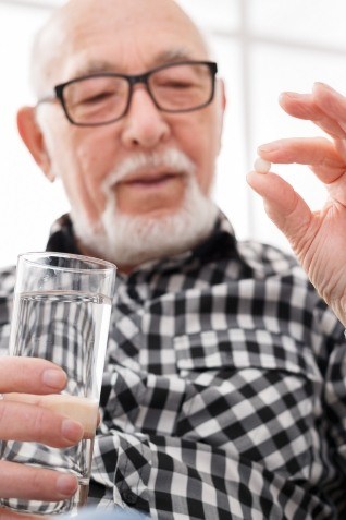 Senior man holding pill and glass of water