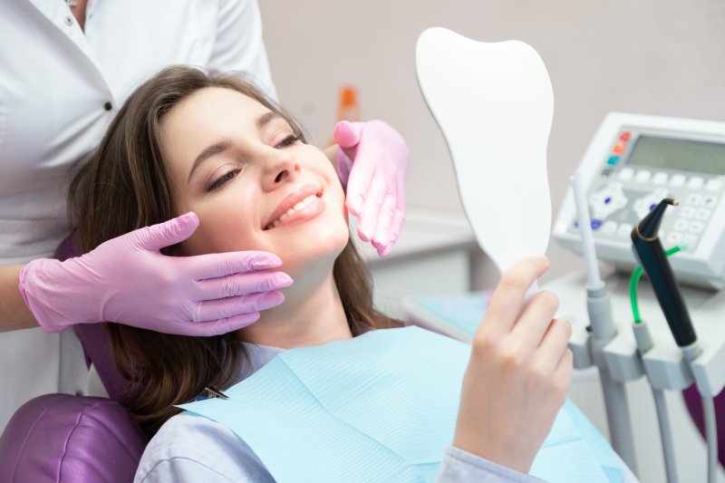A woman smiling in a mirror as she looks at her new cosmetic dentistry treatments