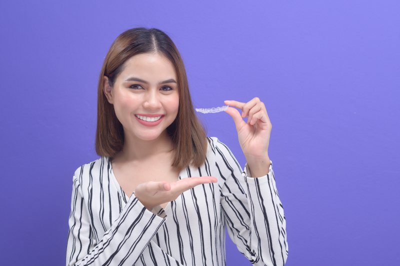 person smiling while holding Invisalign aligner